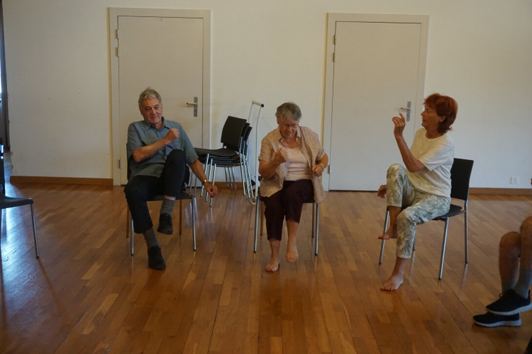 Seniorin macht eine Dehnübung im Sitzen auf dem Stuhl.